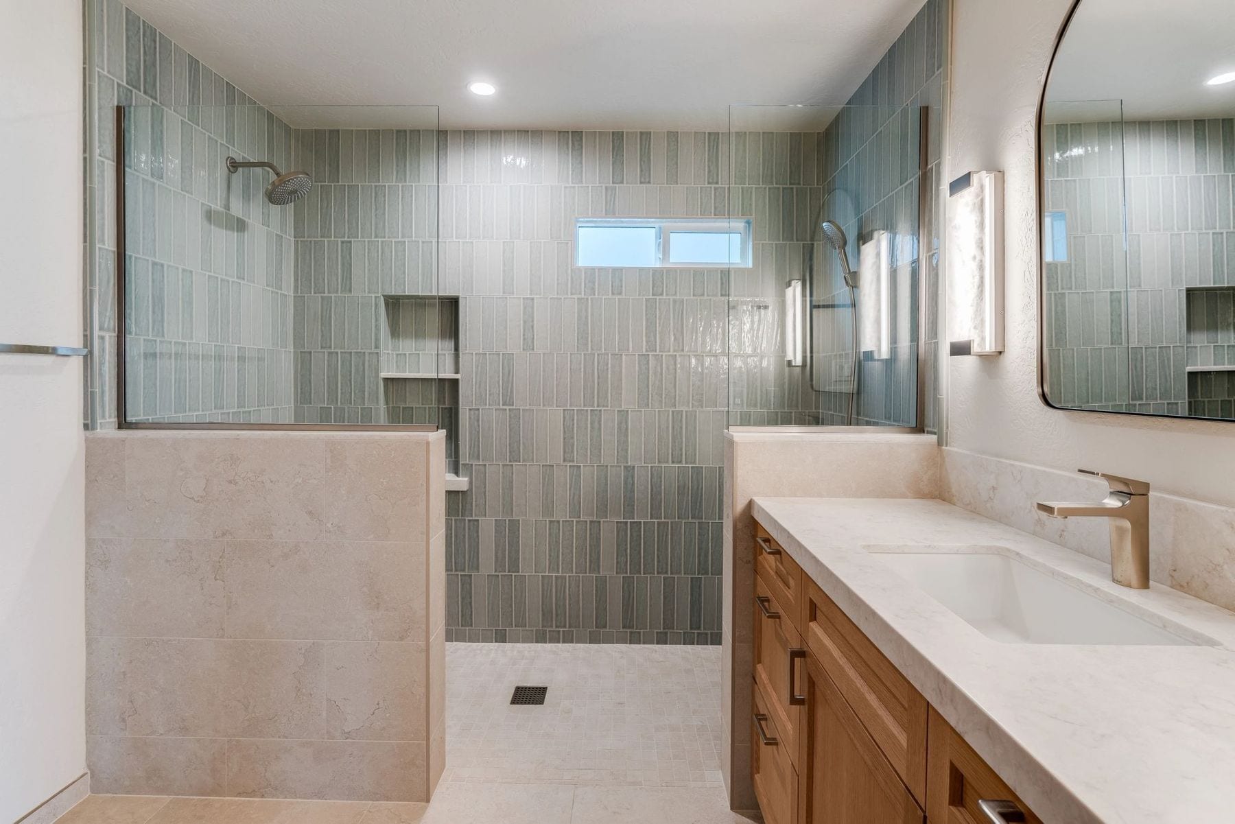 Bathroom with sage-tile shower, wood vanity, and an arched mirror.