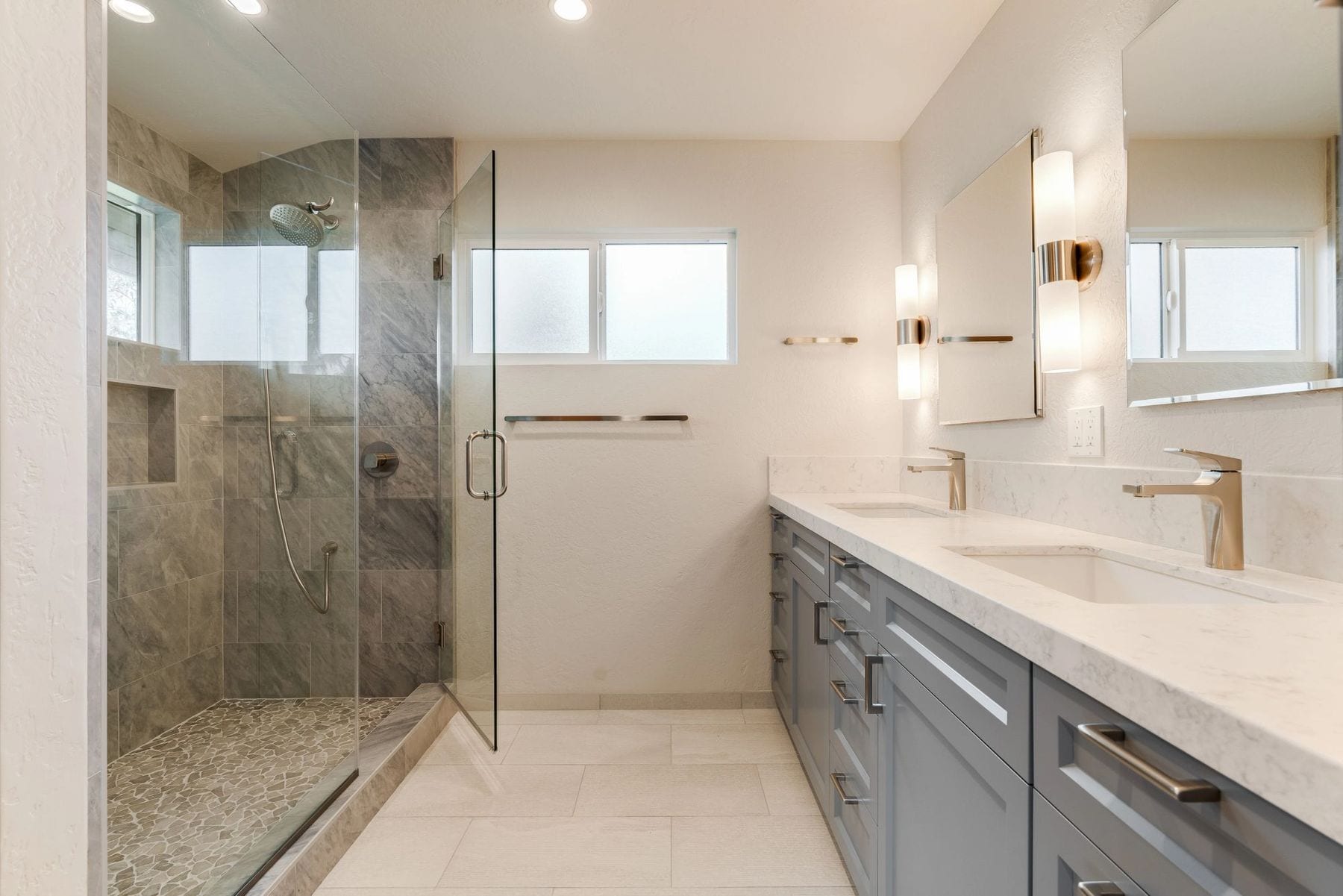 Bathroom with a double vanity, gold fixtures, and a marble-tile glass shower.