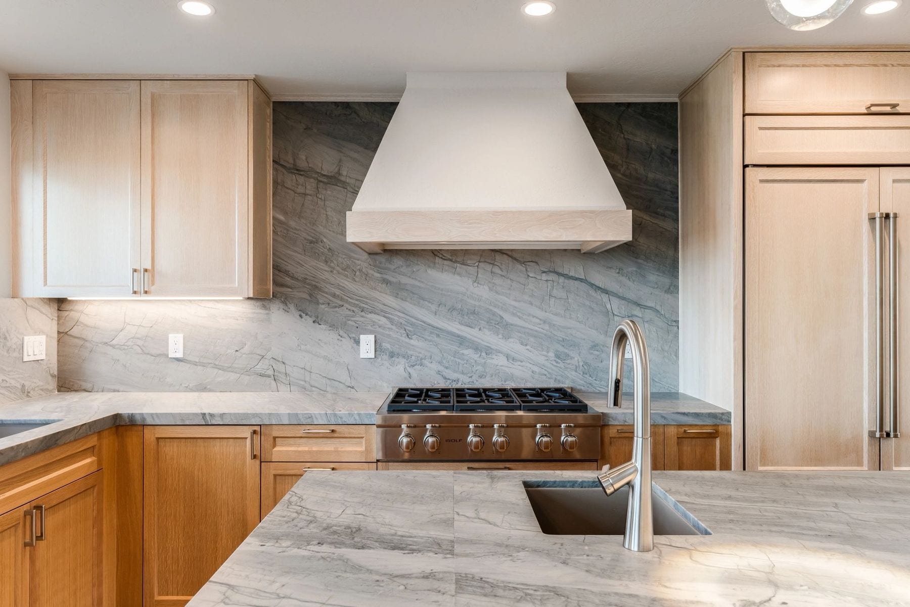 Kitchen with light wood cabinets, veined stone, and a professional gas range.
