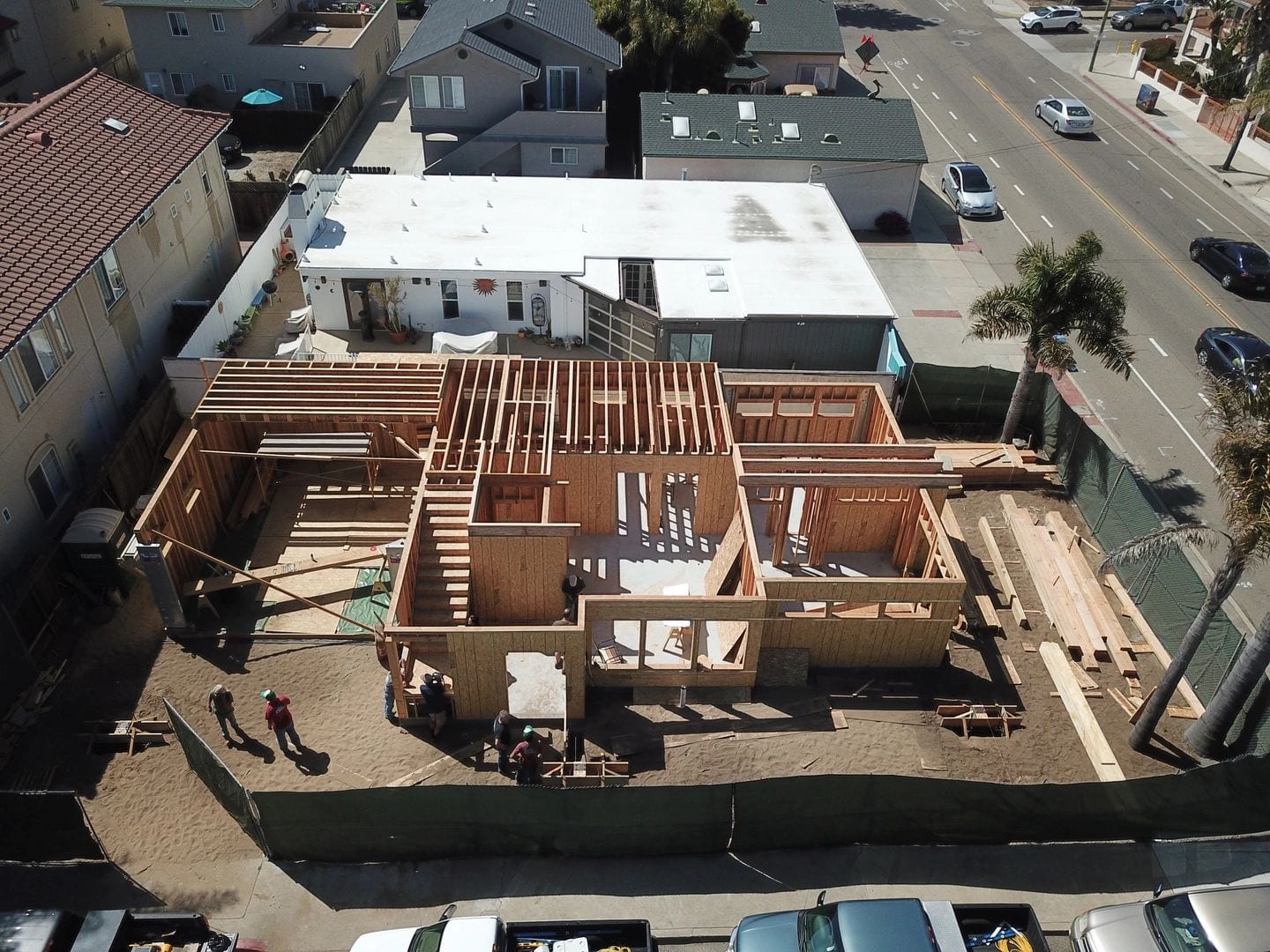 Aerial photograph of a house in framing, with stacked lumber and workers on the lot.