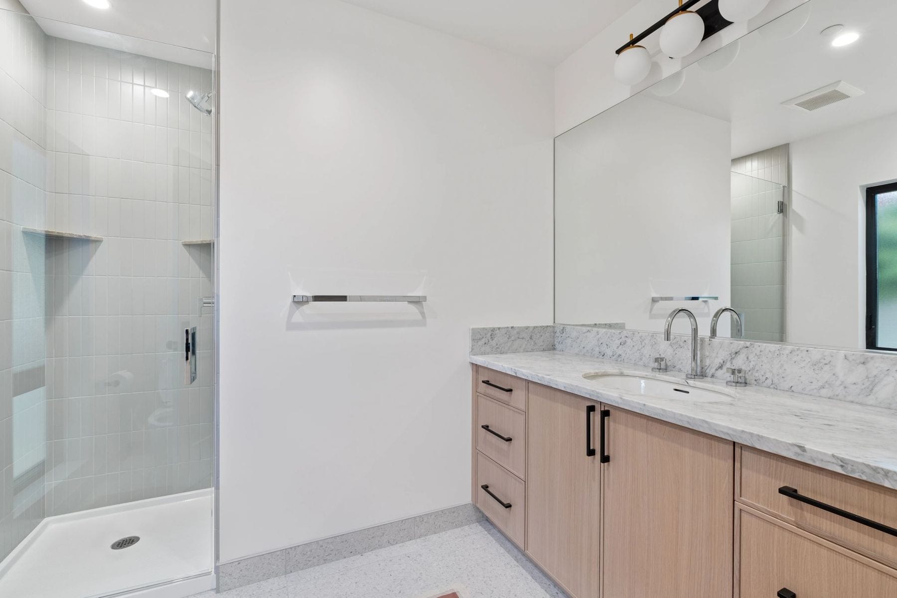 Bathroom with a wood vanity, marble counter, and a glass shower.