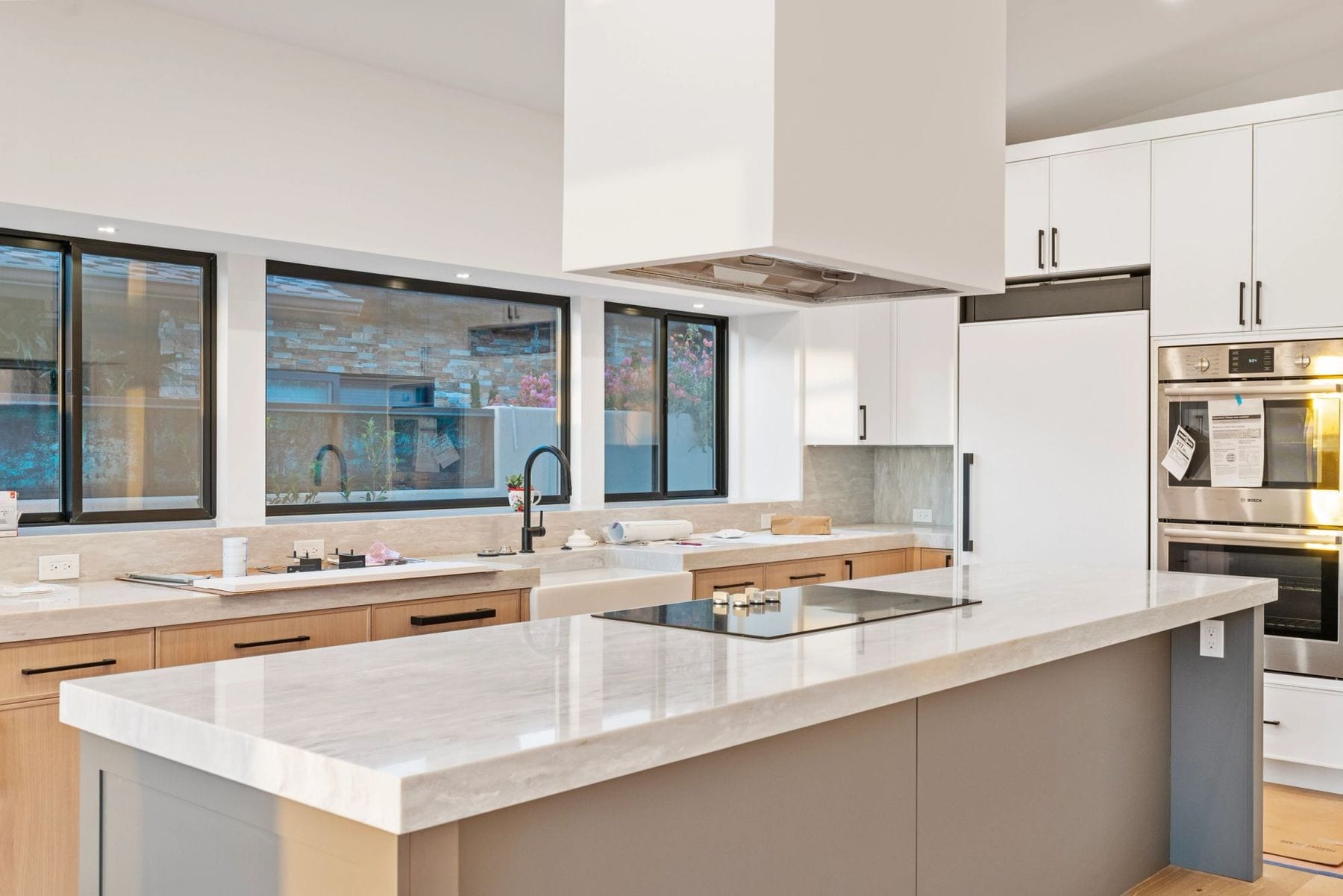 Kitchen with a stone island, white hood, wood cabinets, and black-framed windows.
