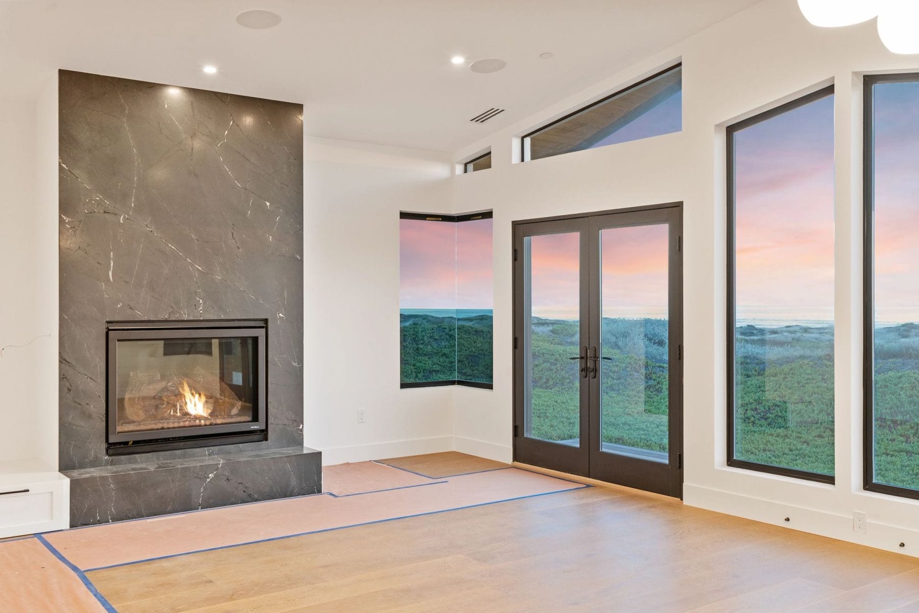 Living room with a dark marble fireplace and glass doors to the ocean at dusk.