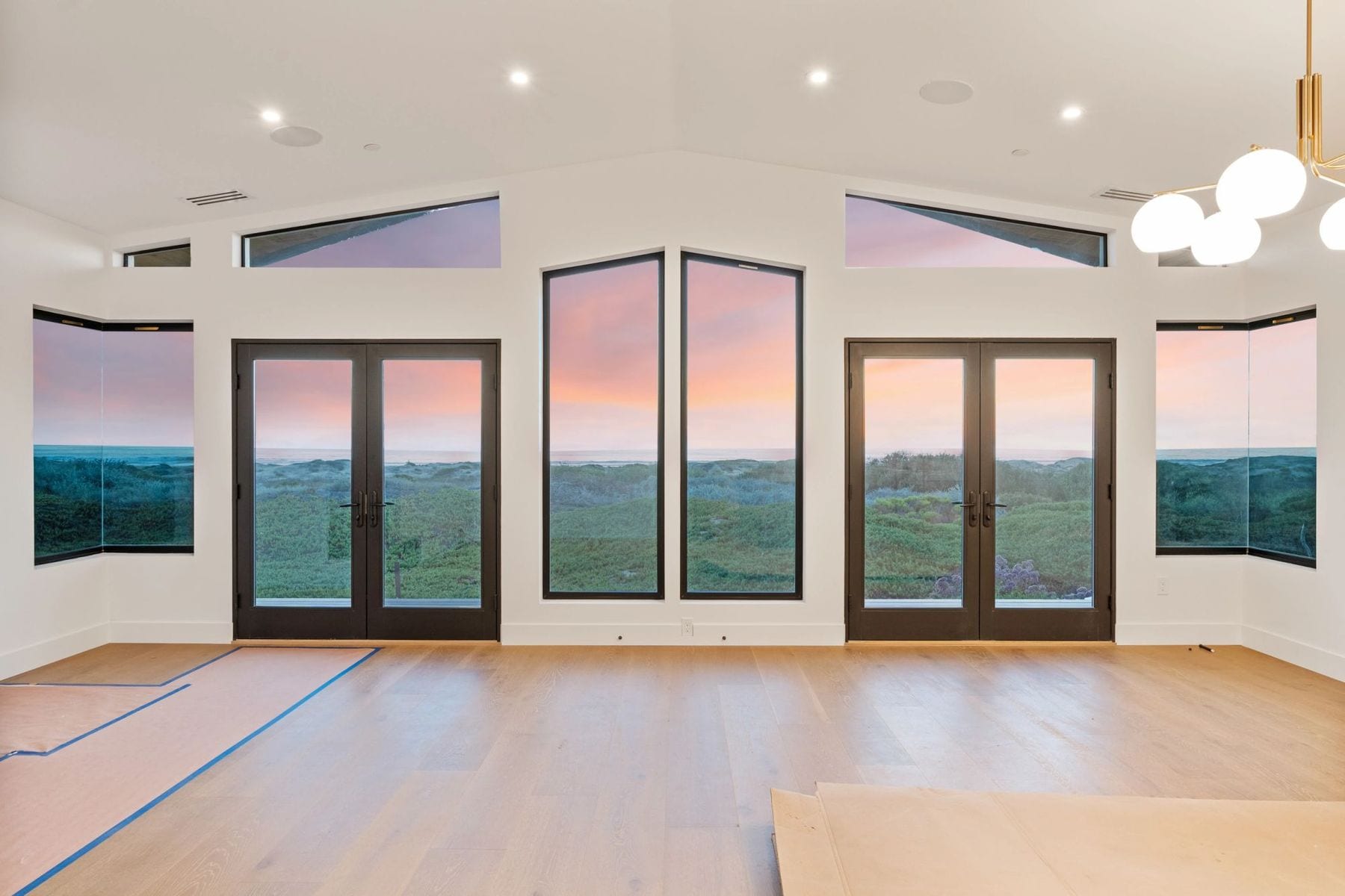 Empty living room with a vaulted ceiling and a wall of glass to the dunes.