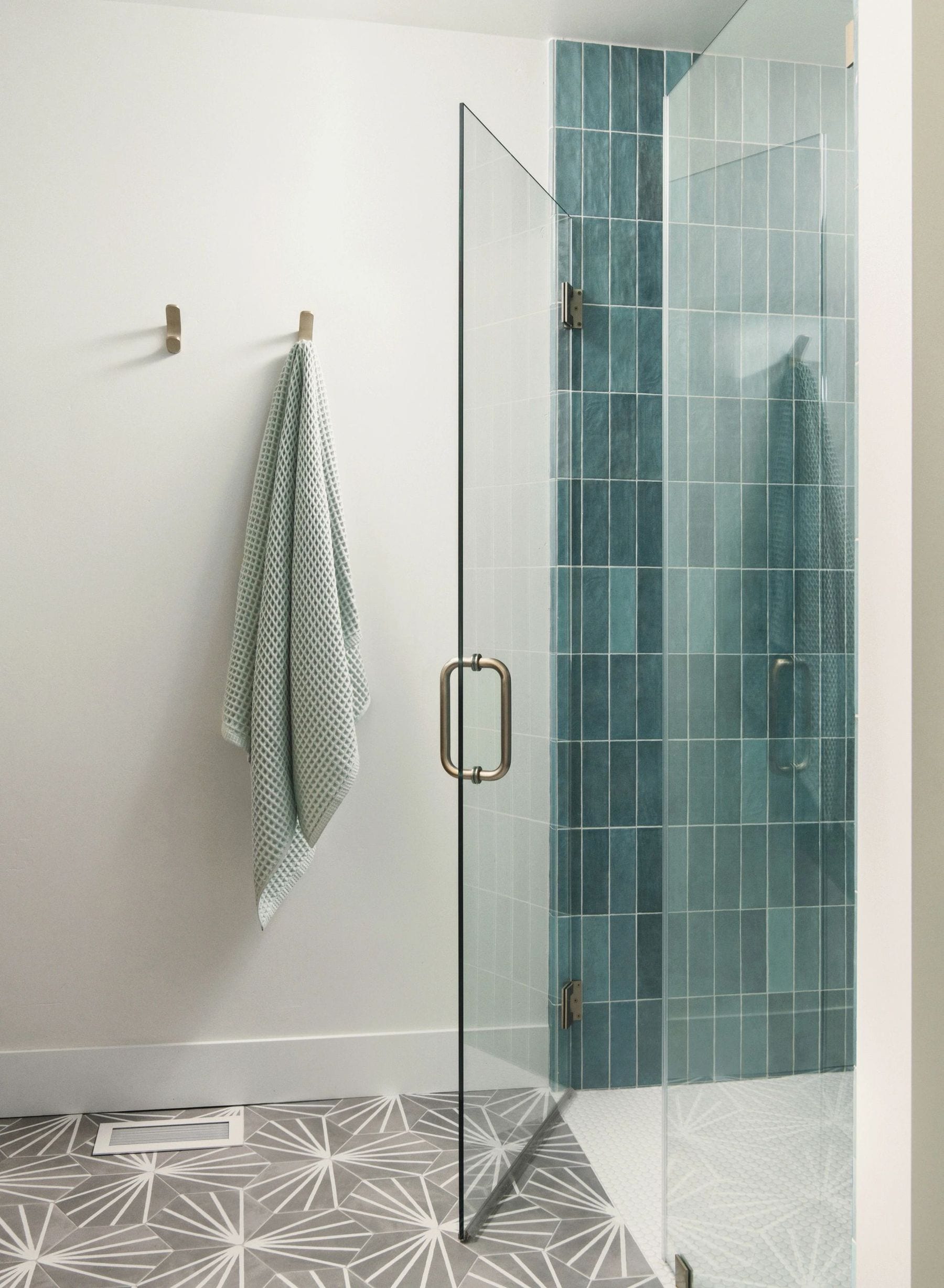 Bathroom shower with teal tile, a glass door, and patterned hexagon floor tile.