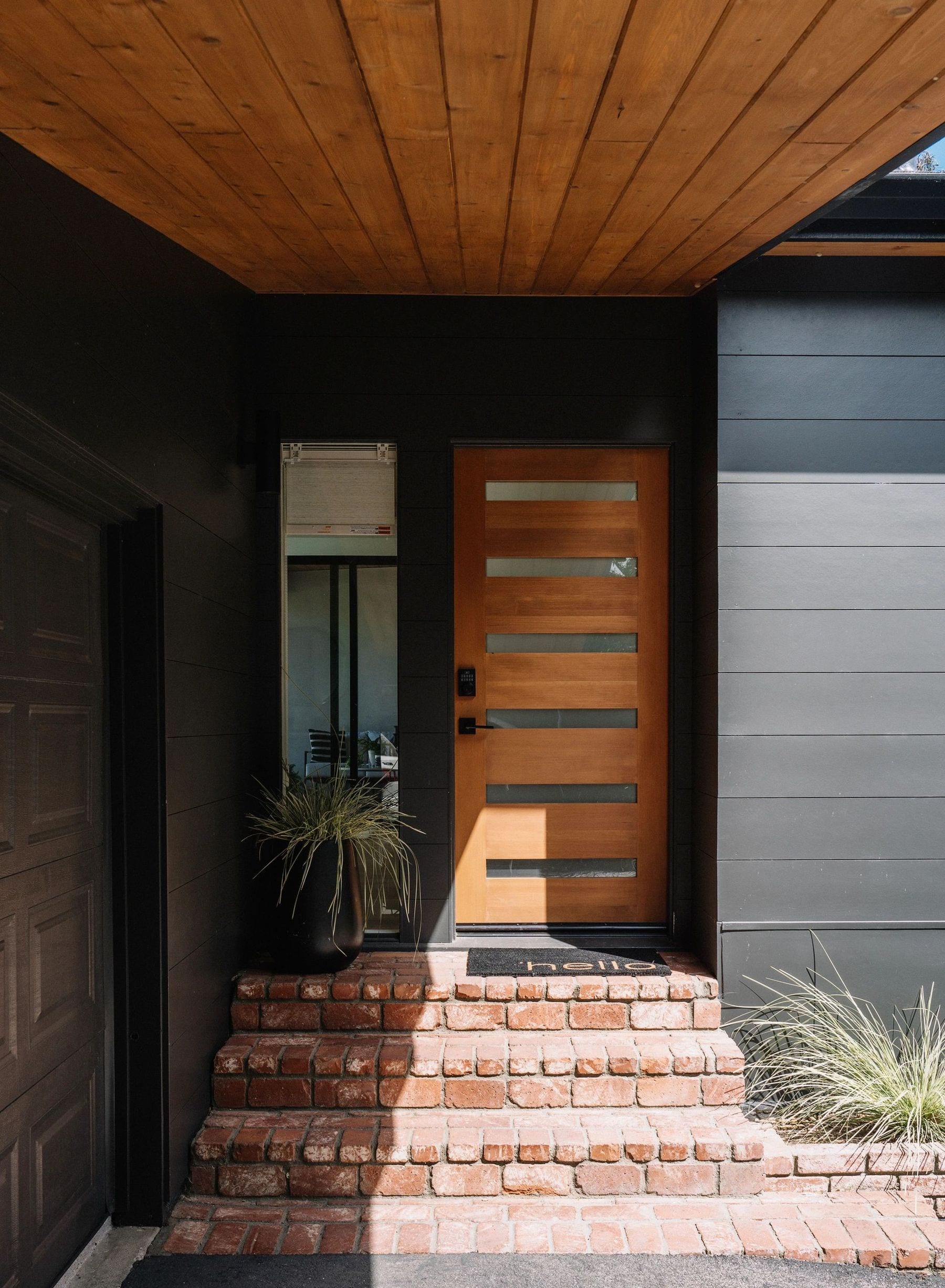 Contemporary house entry with a wood-and-glass door, dark siding, and brick steps.